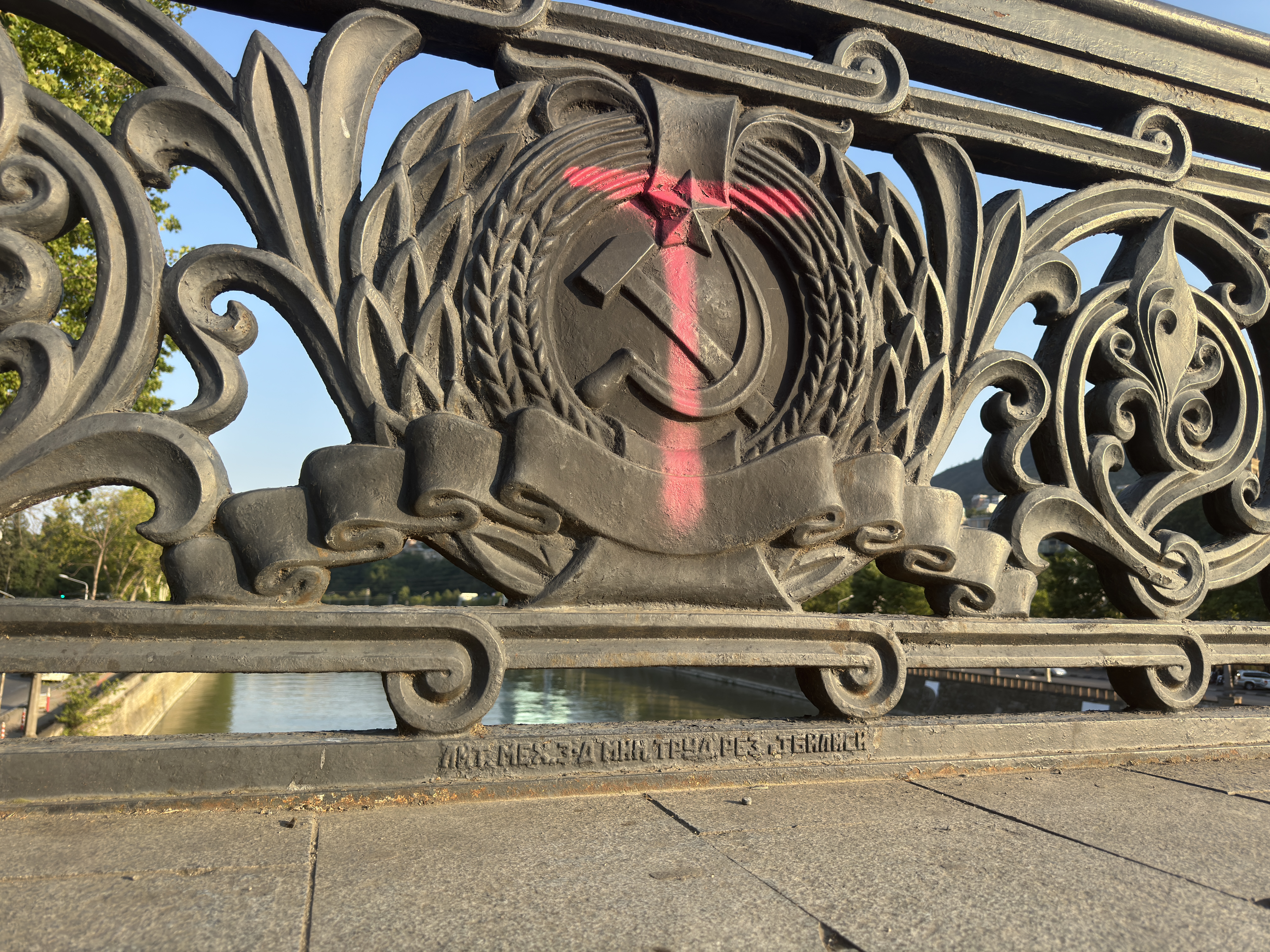Vandalized Soviet hammer and sickle ornament on a bridge railing in Georgia.