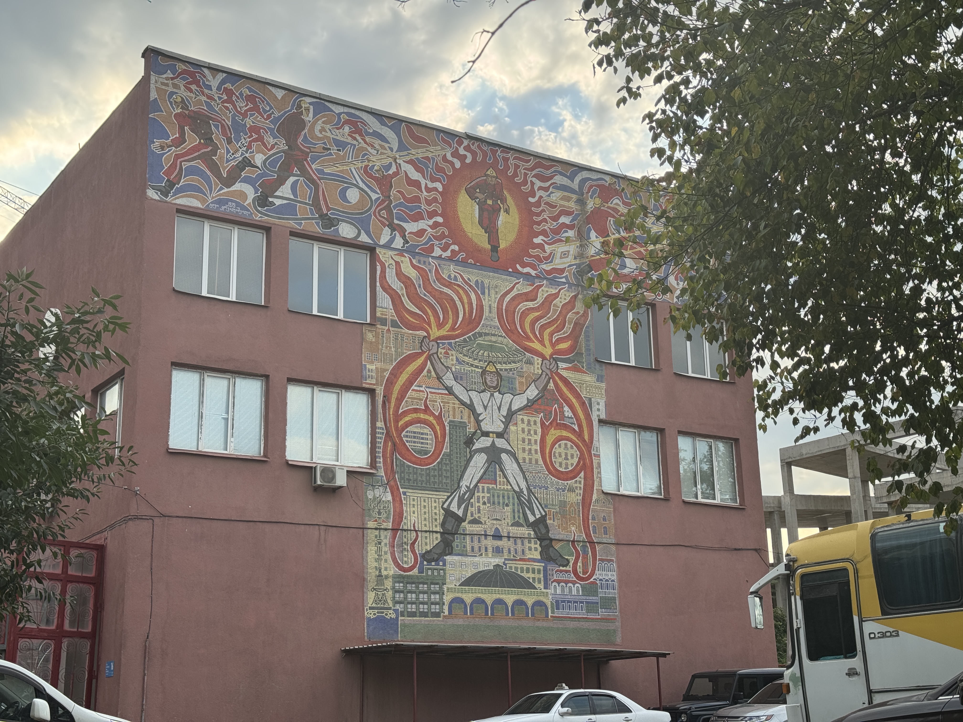 Wide view of the Ortachala fire station showing the full Fire Is in Good Hands mosaic on the building facade in Tbilisi, Georgia.